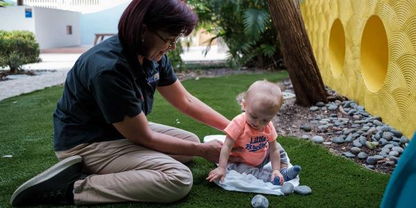 Baby playing with rocks on lawn with educator